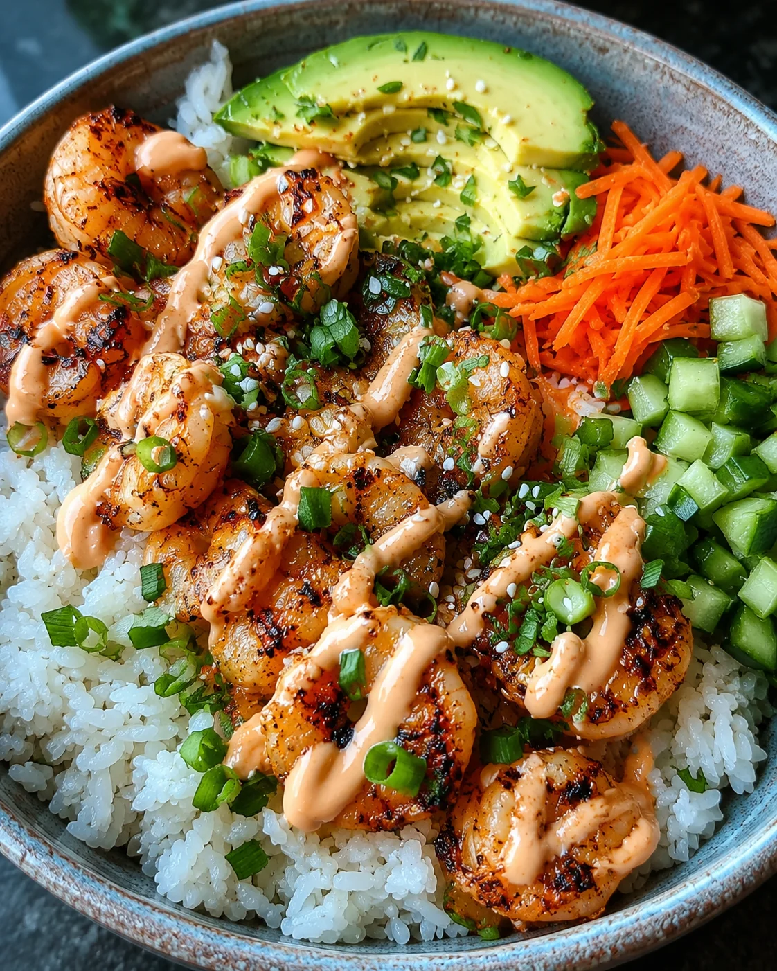 Colorful shrimp rice bowl with avocado, cucumber, carrots, and spicy mayo drizzle
