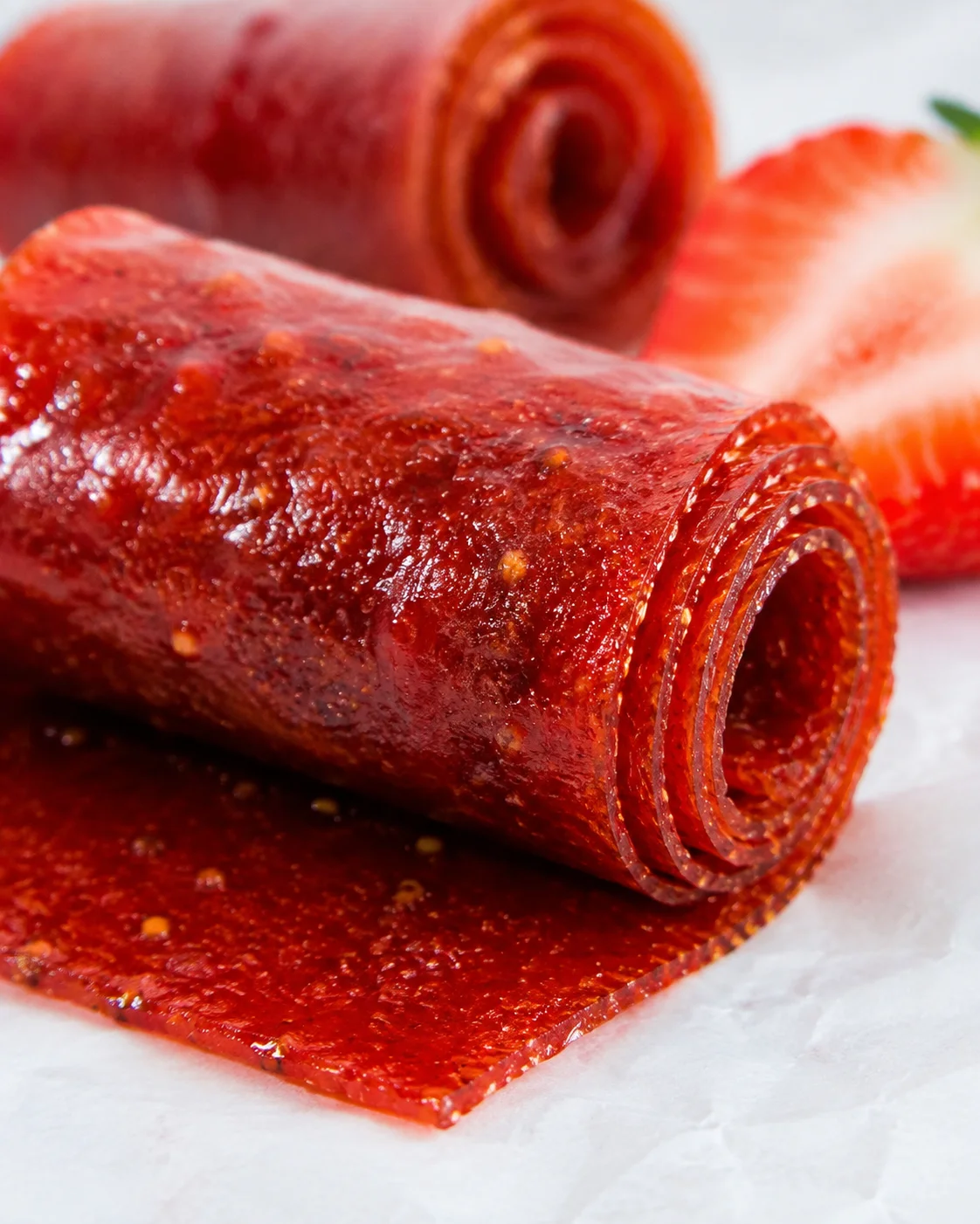 Freshly made strawberry fruit roll-ups on parchment paper with a rolled-up piece nearby.