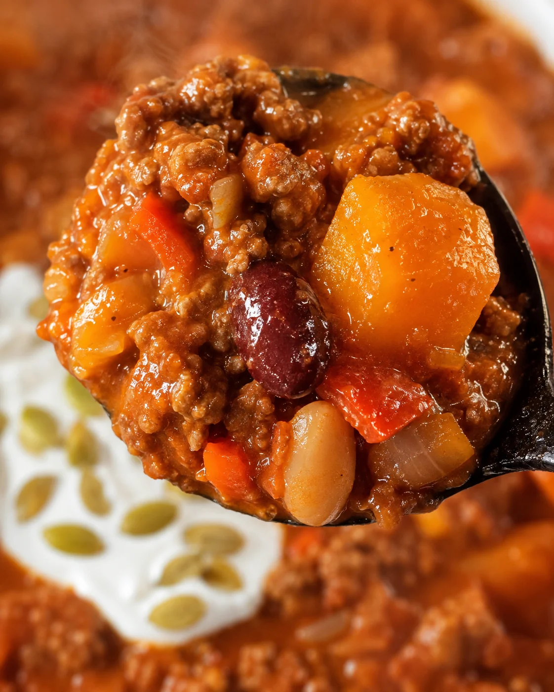 Close-up of a spoonful of rich pumpkin chili with beans and spices.