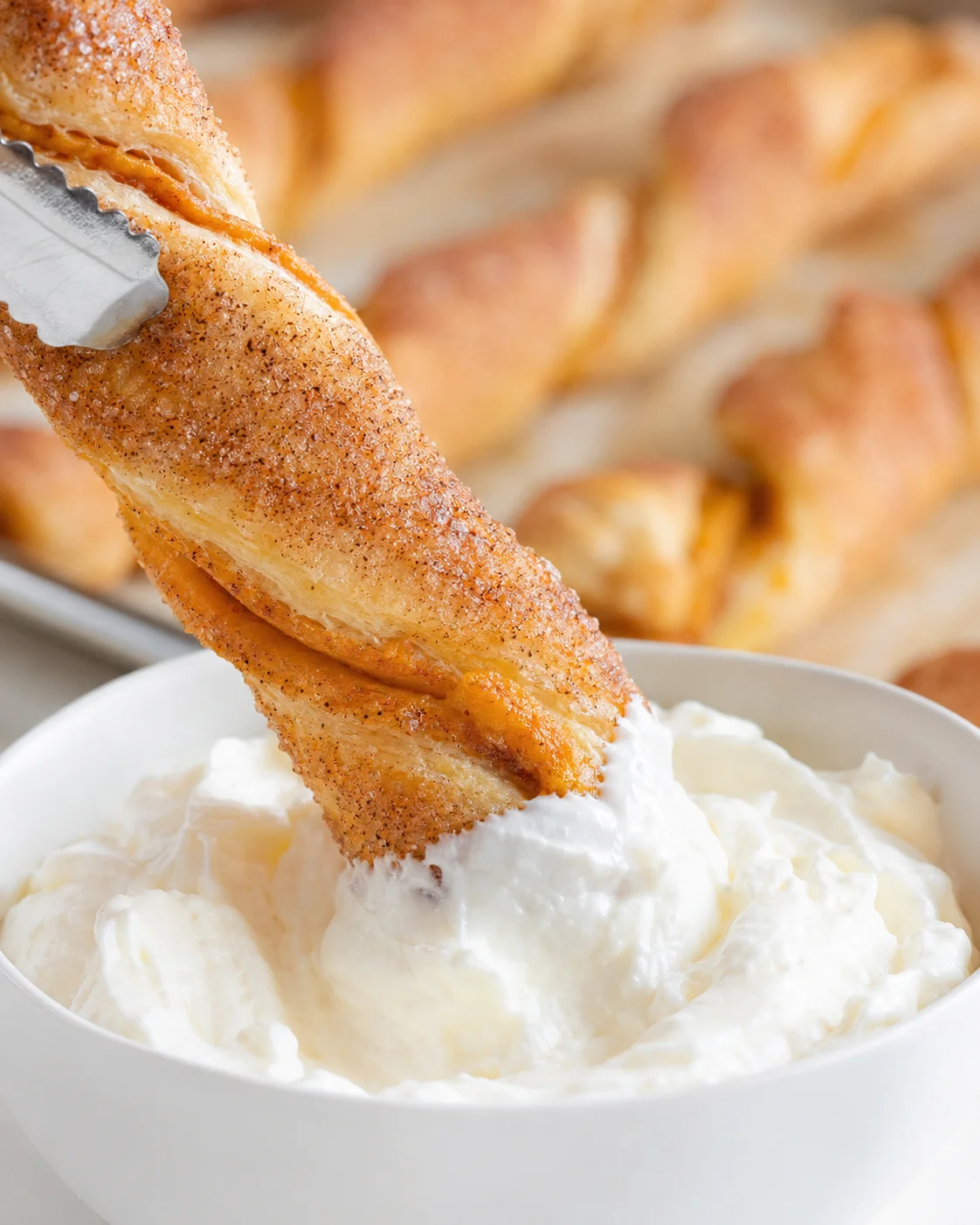 Close-up of a pumpkin pie twist dipped in whipped cream, with a tray of twists in the background.