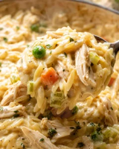 Close-up of creamy chicken pot pie orzo with vegetables and shredded chicken on a spoon