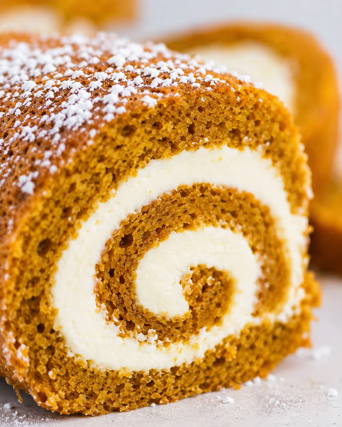 Close-up of a sliced pumpkin roll with cream cheese filling and powdered sugar